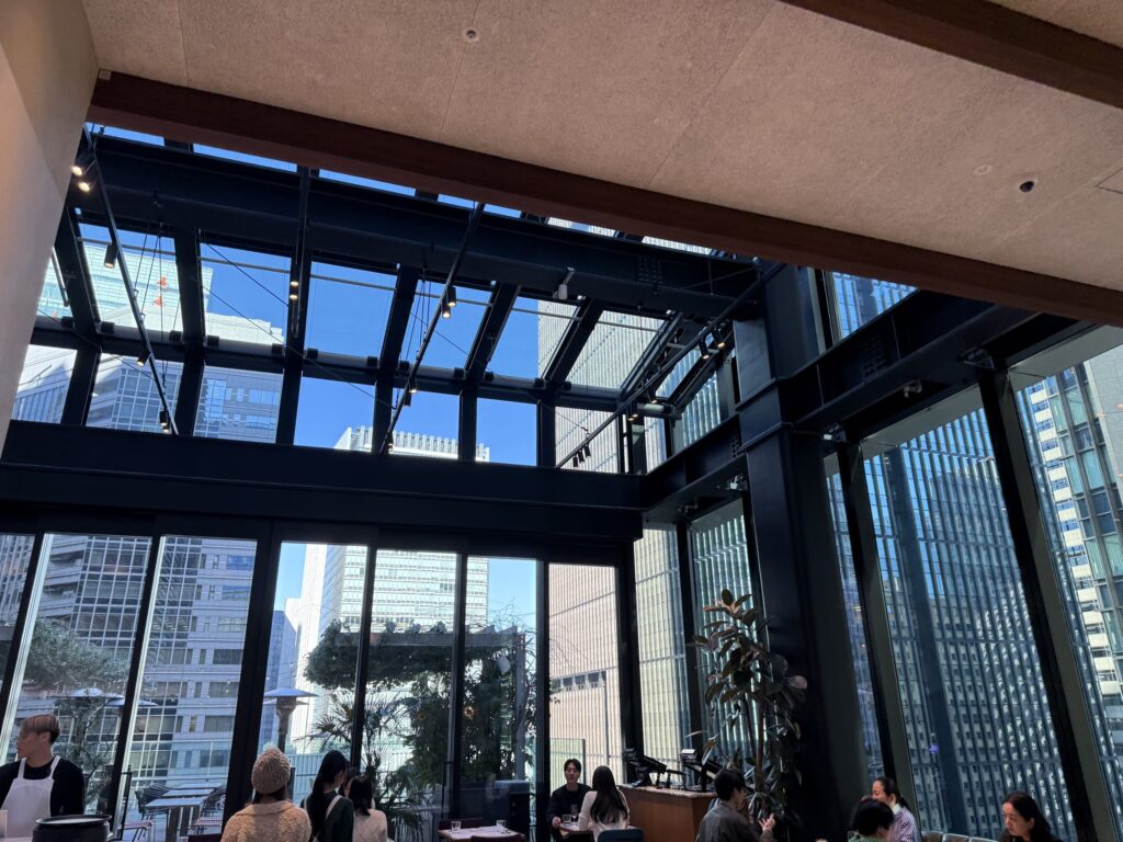 高い天井と黒い鉄骨の天窓から青空が見える、丸の内のレストランの開放的な店内風景