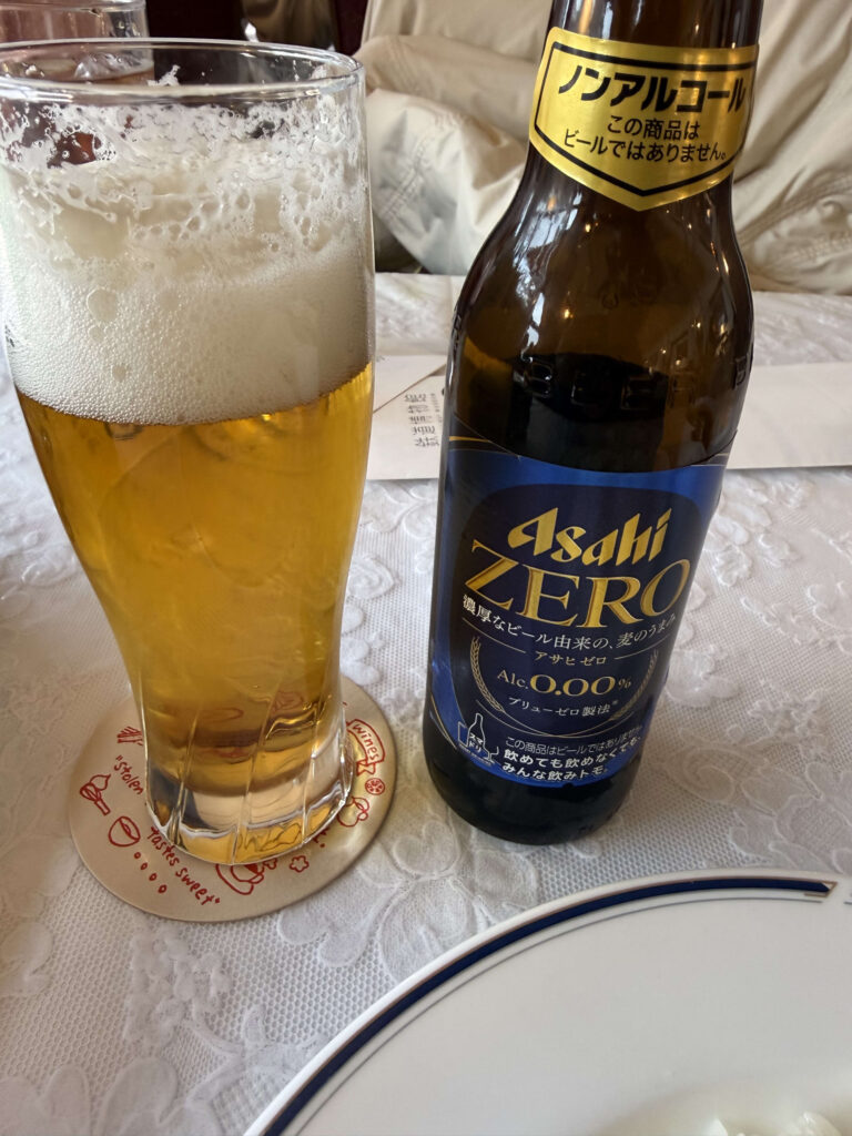A bottle of Asahi ZERO non-alcoholic beer and a glass filled with golden liquid and white foam on a white tablecloth