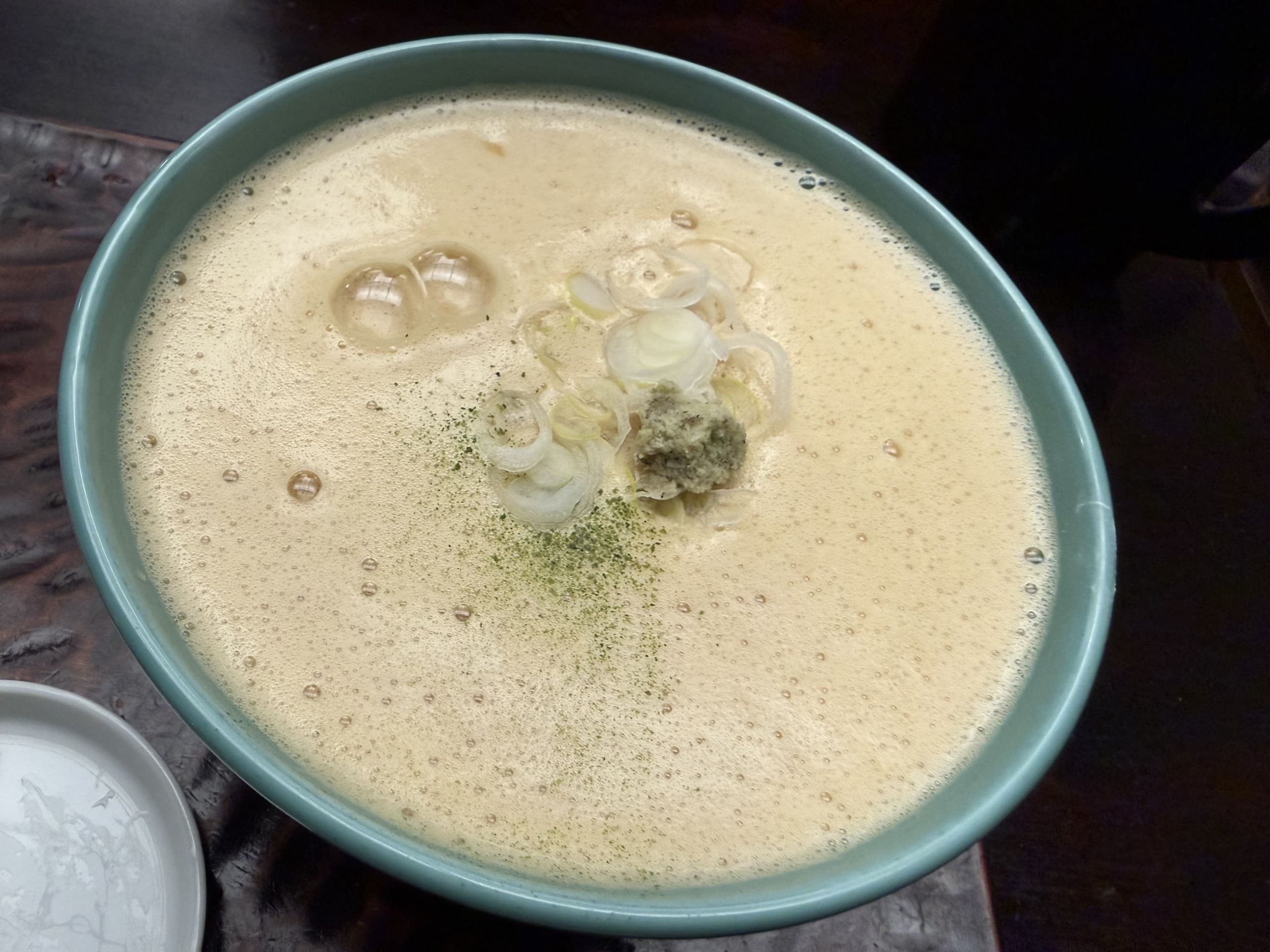 白いクリーミーな泡に覆われ、ネギとワサビがトッピングされたカレーうどん