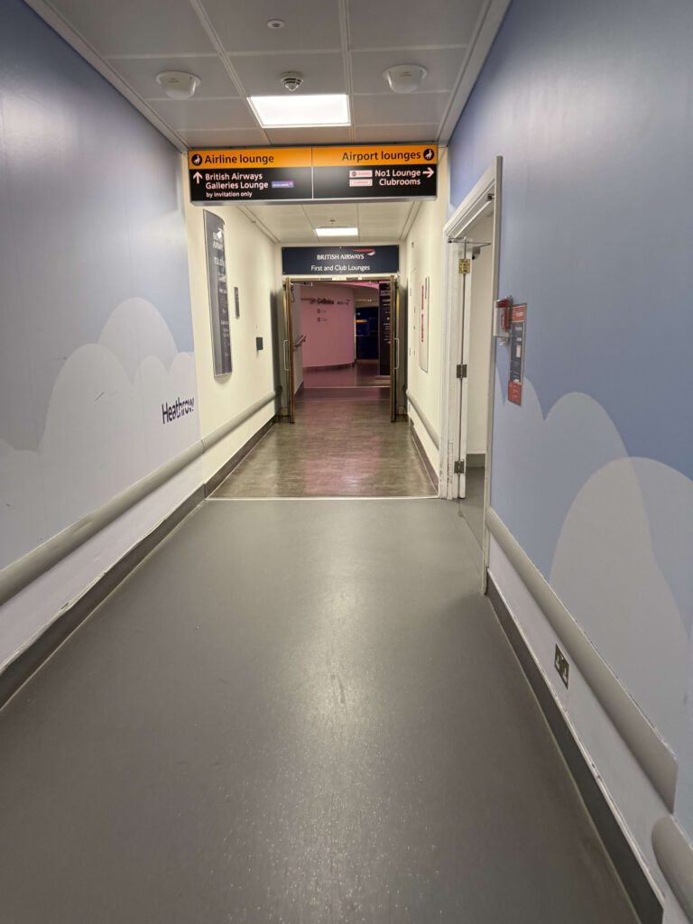 Hallway at Heathrow Airport with cloud-patterned walls leading to the British Airways First and Club Lounges entrance