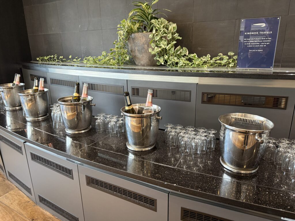 Champagne and sparkling wine bottles chilling in silver ice buckets on a sleek black counter in an airport lounge