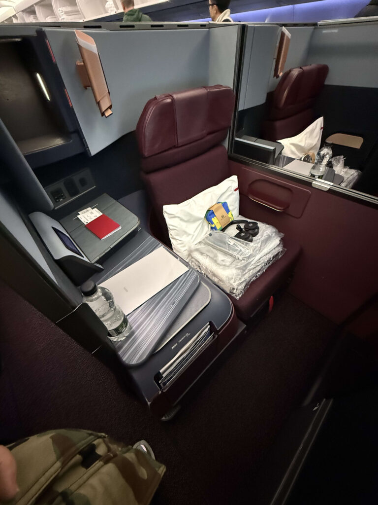 JAL SKY SUITEのビジネスクラス座席。バーガンディ色のシートに枕、ヘッドフォン、アメニティが置かれている。
