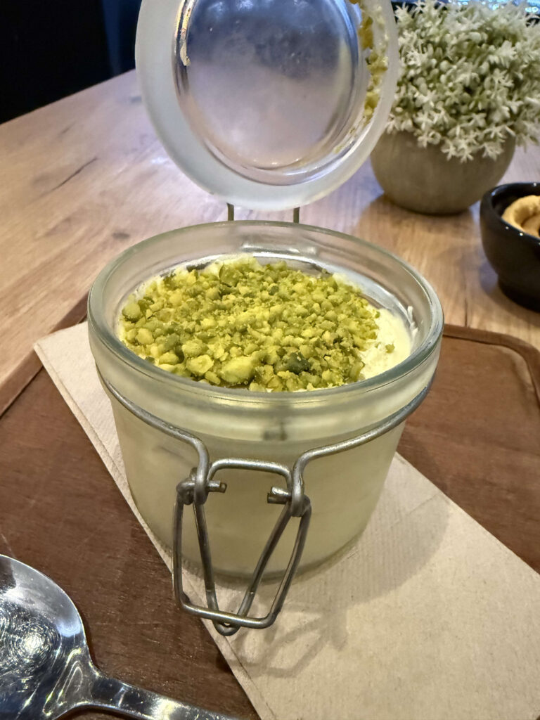 蓋が開いたガラス瓶に入り、砕いたピスタチオがトッピングされたティラミス
