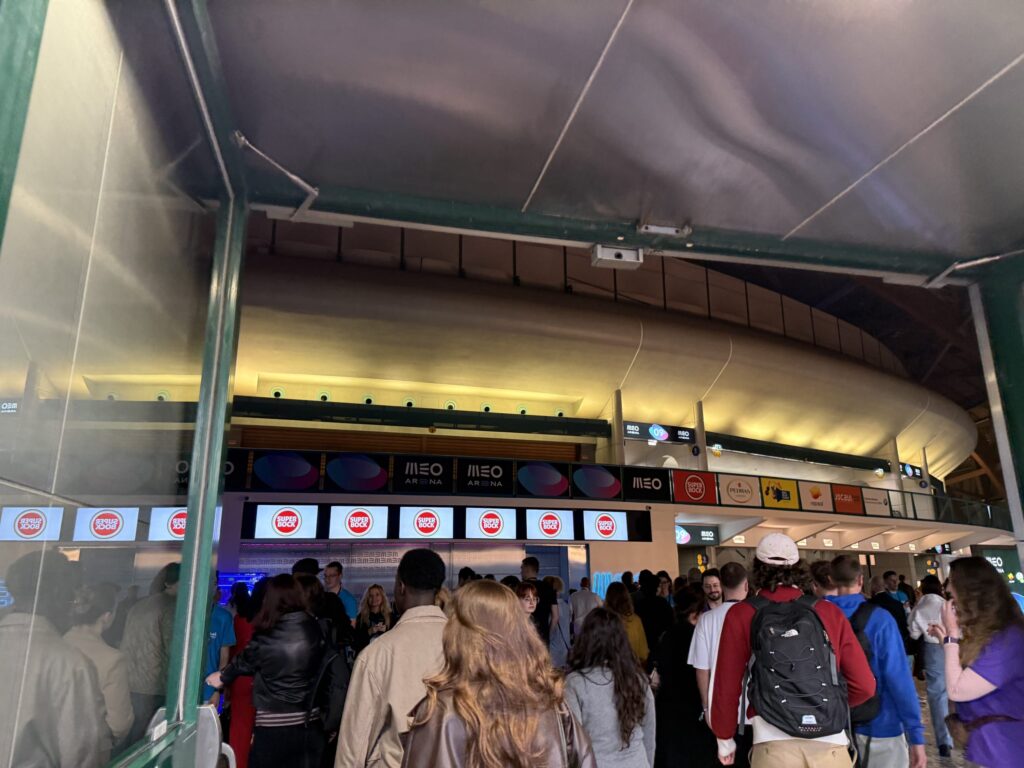Crowd of people walking through the MEO Arena concourse under Super Bock digital signs