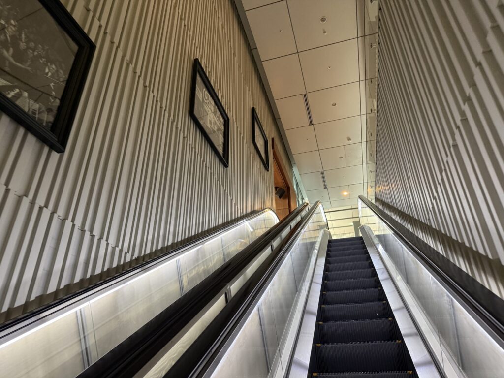 TOKIAビルの1階から2階へ続くエスカレーターと、縦縞の壁に飾られた額縁アートを見上げた構図
