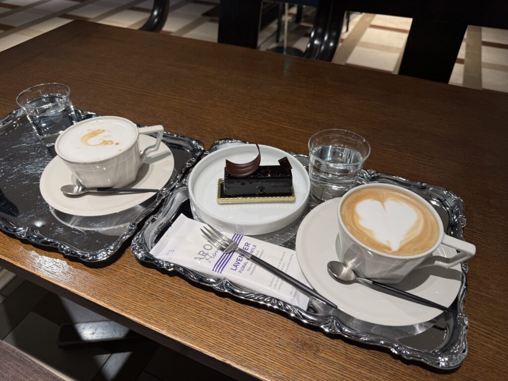 木製のテーブルに置かれた銀のトレイ上のデカフェカプチーノ、ラテ、そしてミロワールショコラ