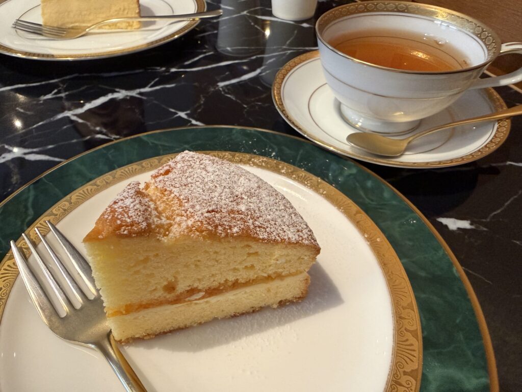 Victoria sponge cake on a green and gold rimmed plate next to a cup of tea