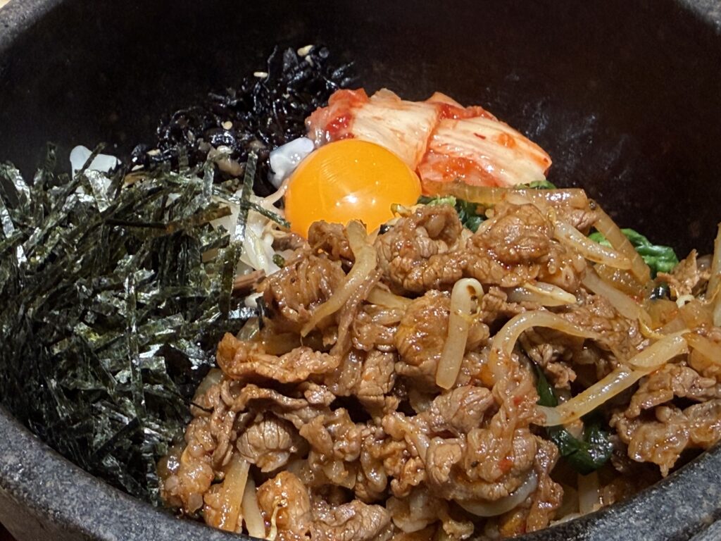 Close-up of Bibimbap in a stone bowl featuring beef bulgogi, kimchi, seaweed, and a raw egg yolk