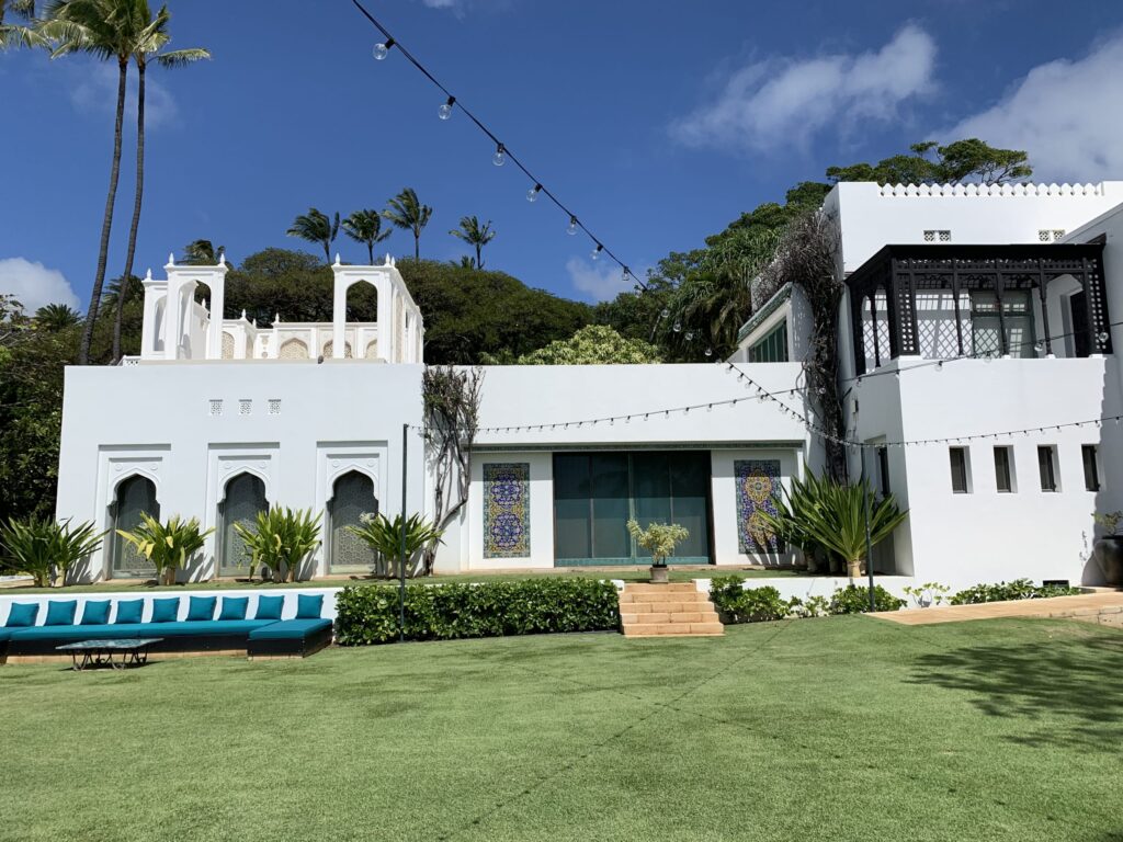 青空の下、アーチ型の窓と白い壁が特徴的な邸宅と緑の芝生