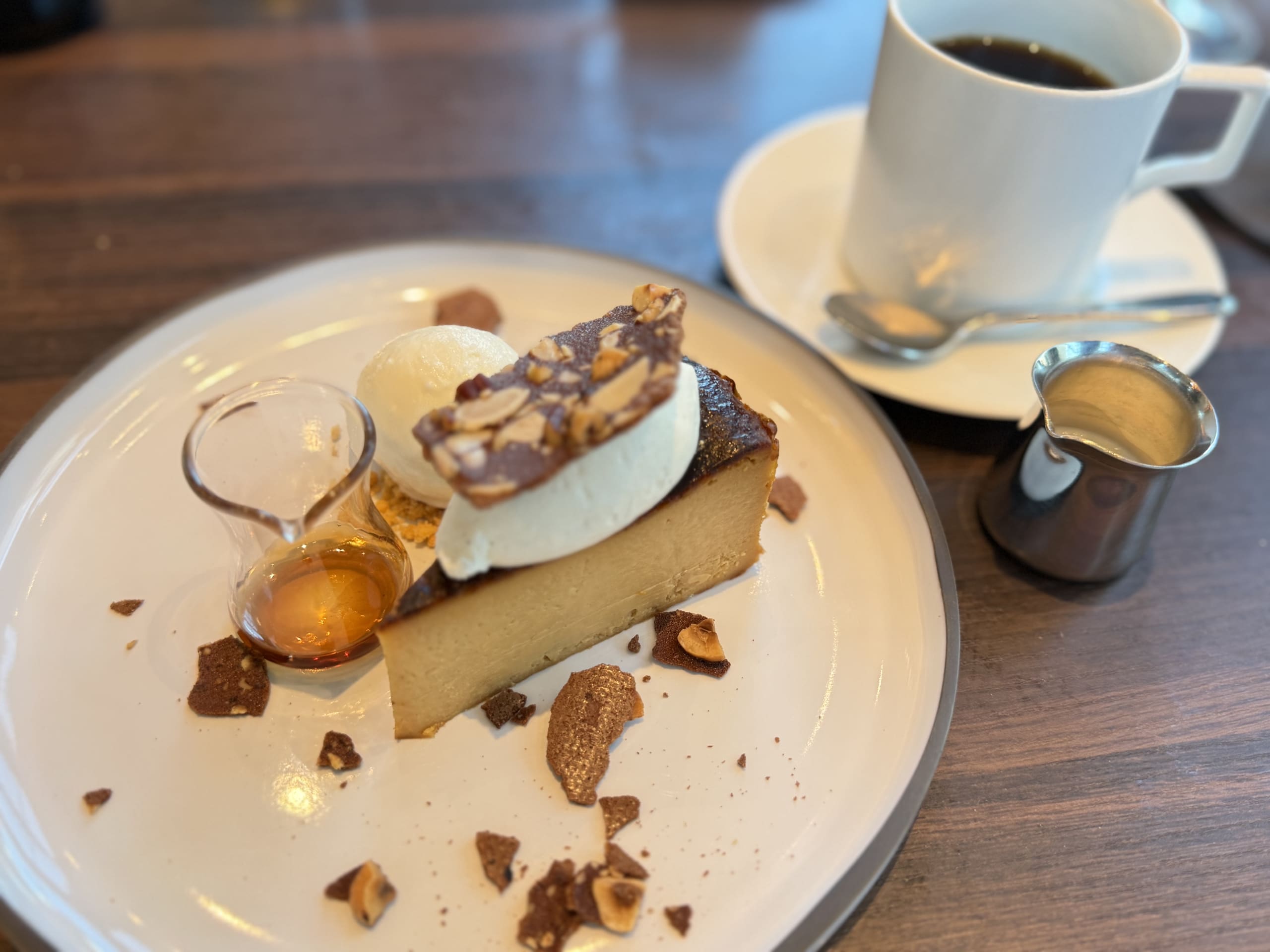 Caramel Basque Cheesecake topped with cream and nut brittle, served with ice cream, syrup, and a cup of black coffee.