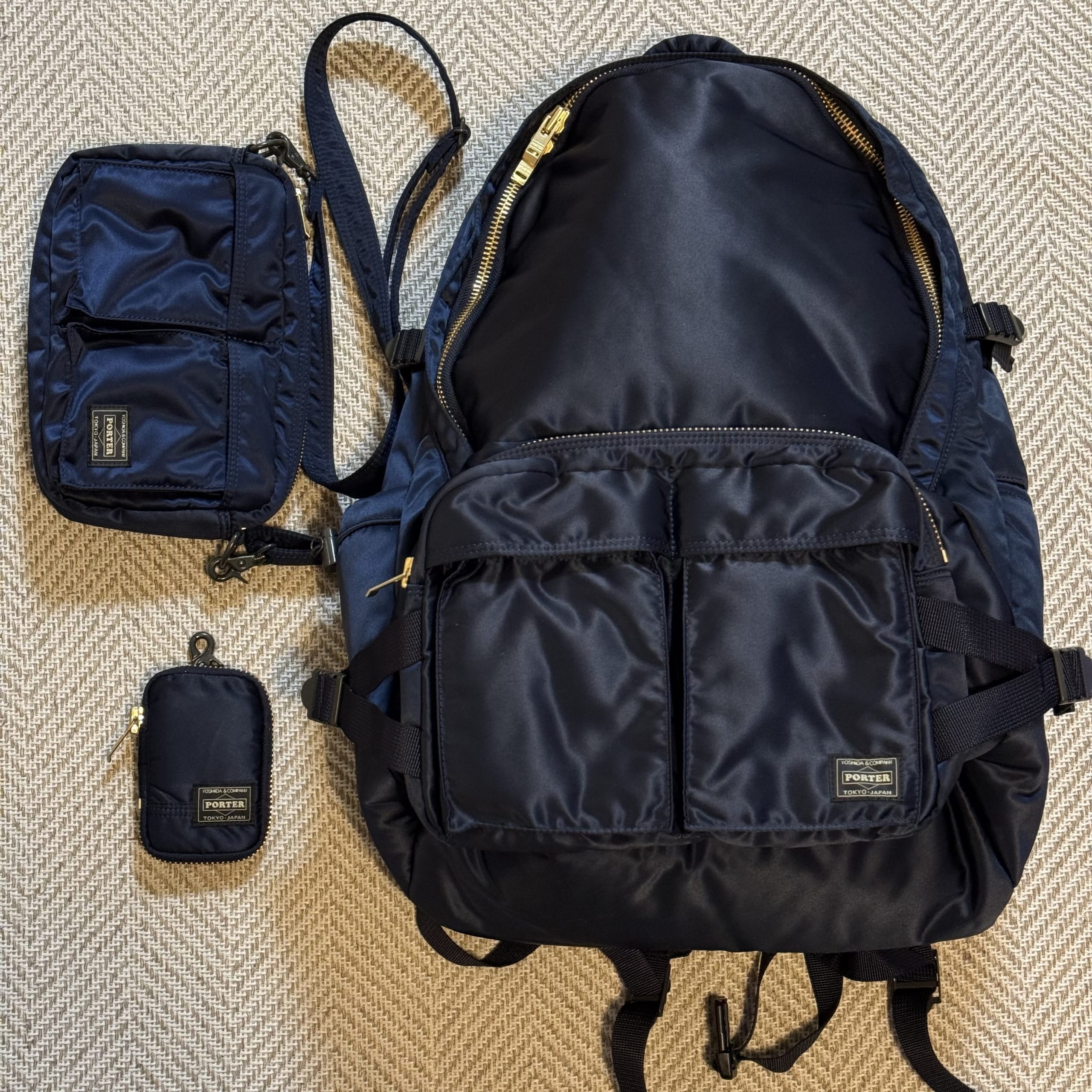 PORTER（ポーター）タンカーシリーズ「アイアンブルー」のバックパック、ショルダーバッグ、ポーチの3点がカーペットの上に並べられた俯瞰写真