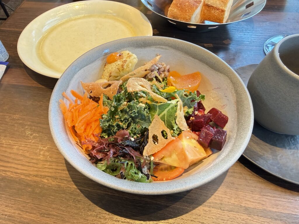 A colorful Buddha bowl filled with fresh vegetables, grains, and lotus root chips on a wooden table