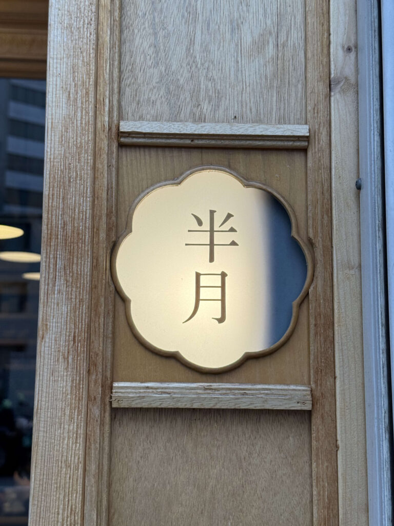 Flower-shaped brass sign plate engraved with the Japanese text 'Hangetsu' embedded in a wooden pillar