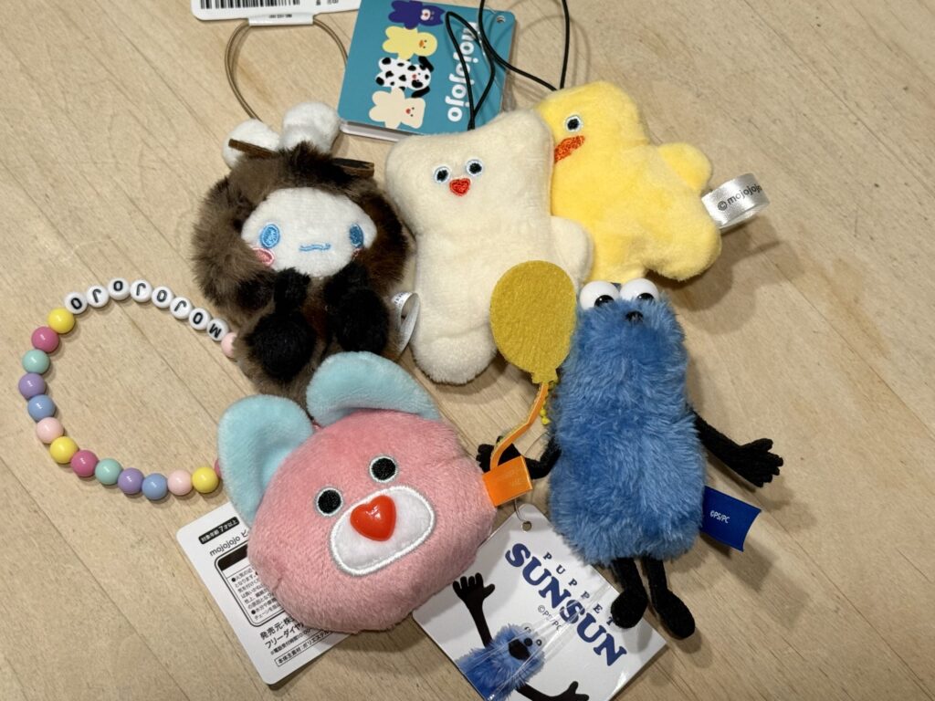 Plush toys of Puppet Sunsun, mojojojo characters, and Cinnamoroll arranged with a beaded bracelet on wood
