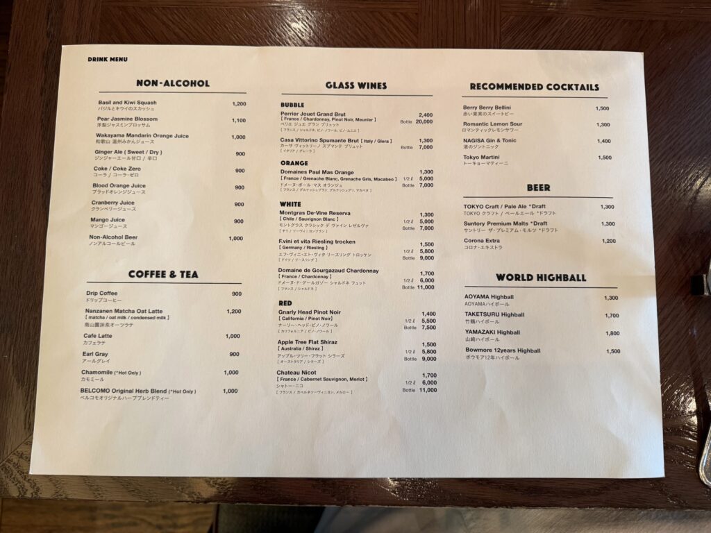 A printed drink menu listing non-alcoholic drinks, wines, cocktails, beer, coffee, tea, and highballs on a wooden table
