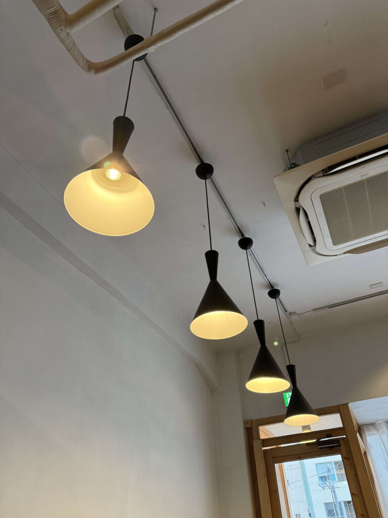 Four black cone-shaped pendant lights hanging from a white industrial ceiling with exposed pipes