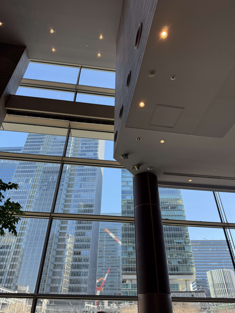 Looking up at skyscrapers and construction cranes near Tokyo Station through a massive glass window from a modern interior with high ceilings