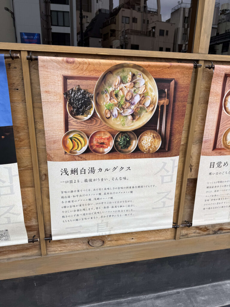 Advertisement tapestry for Clam Paitan Kalguksu displayed at a restaurant entrance