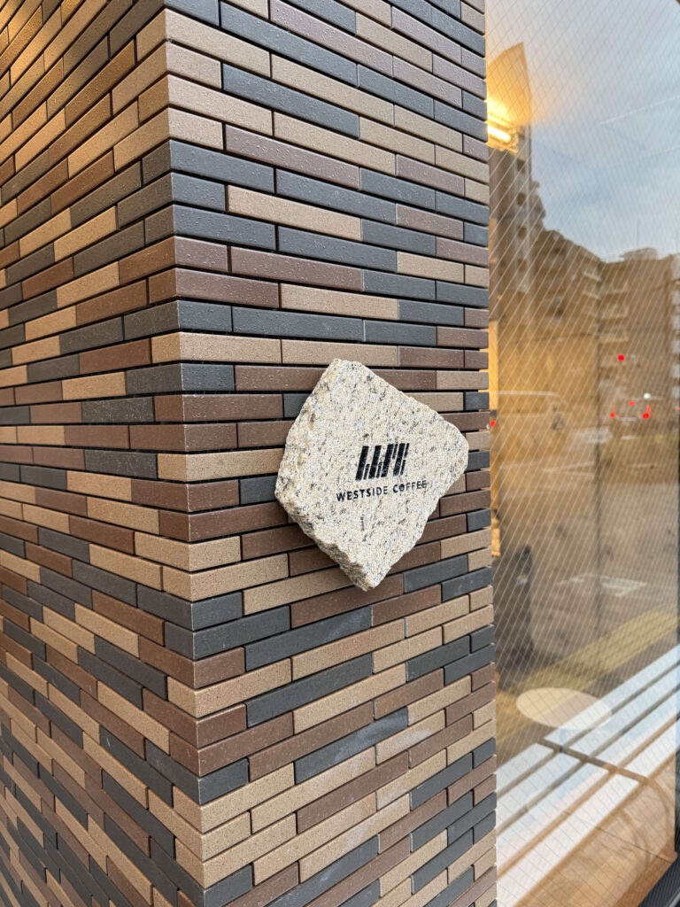 Diamond-shaped stone signage with the Westside Coffee logo mounted on a brown and grey brick wall