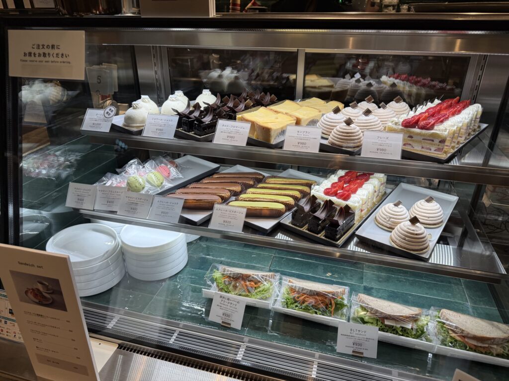 A cafe display case filled with an assortment of colorful cakes, eclairs, and sandwiches.