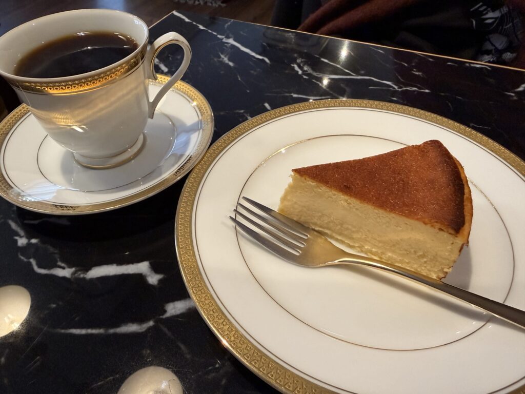 黒いマーブル模様のテーブルに置かれたバスクチーズケーキと金縁のカップに入ったコーヒー