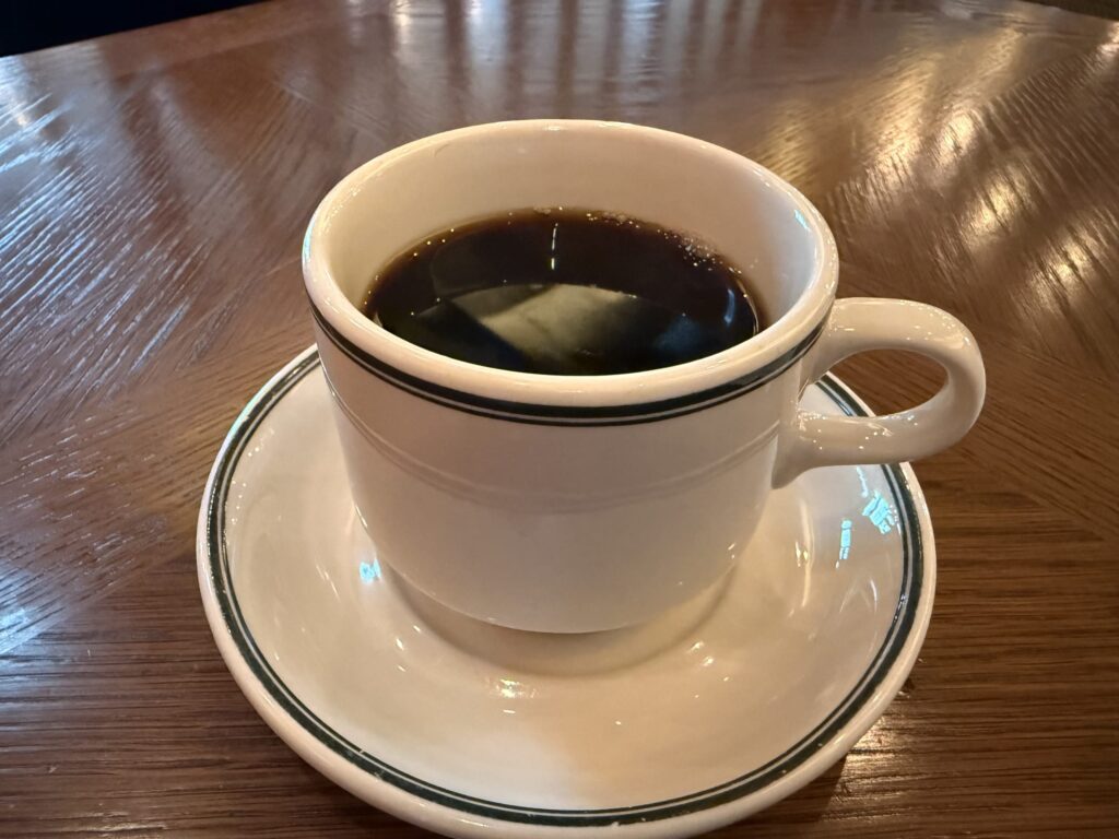 木製のテーブルに置かれた、緑のラインが入った白いカップとソーサーに注がれたホットコーヒー