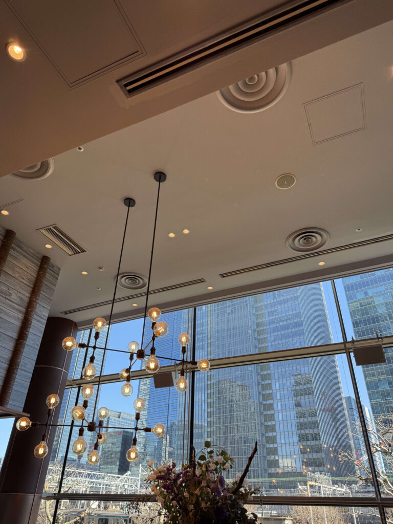 Modern branching chandelier hanging from a high ceiling with Marunouchi skyscrapers visible through large windows