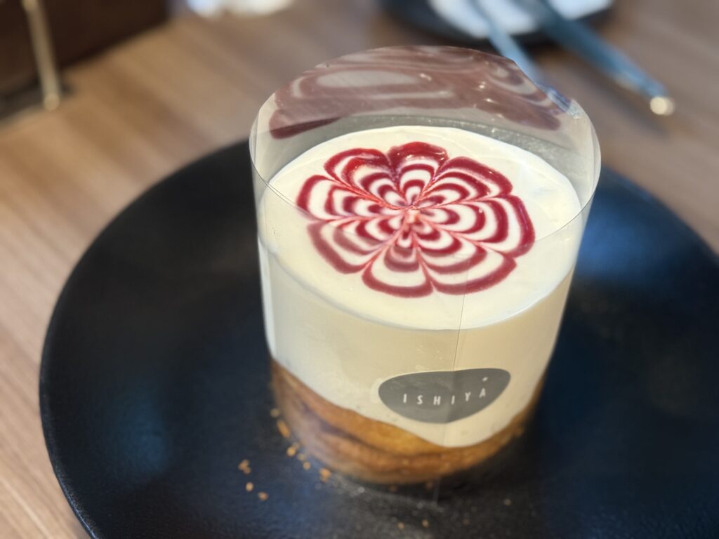 黒い皿に乗せられた、透明なフィルムで包まれたISHIYAのパンケーキとクリーム上の赤い花の模様