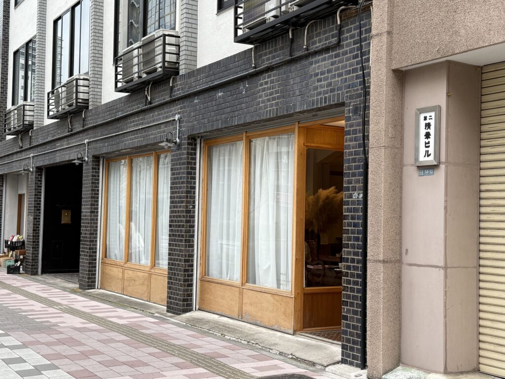 Exterior of the Daini Seika Bill 1st floor featuring retro brick tiles, wooden window frames, and white curtains