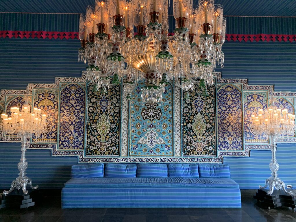 Interior of the Tent Room featuring a massive crystal chandelier, intricate blue floral wall patterns, and a long blue striped sofa.