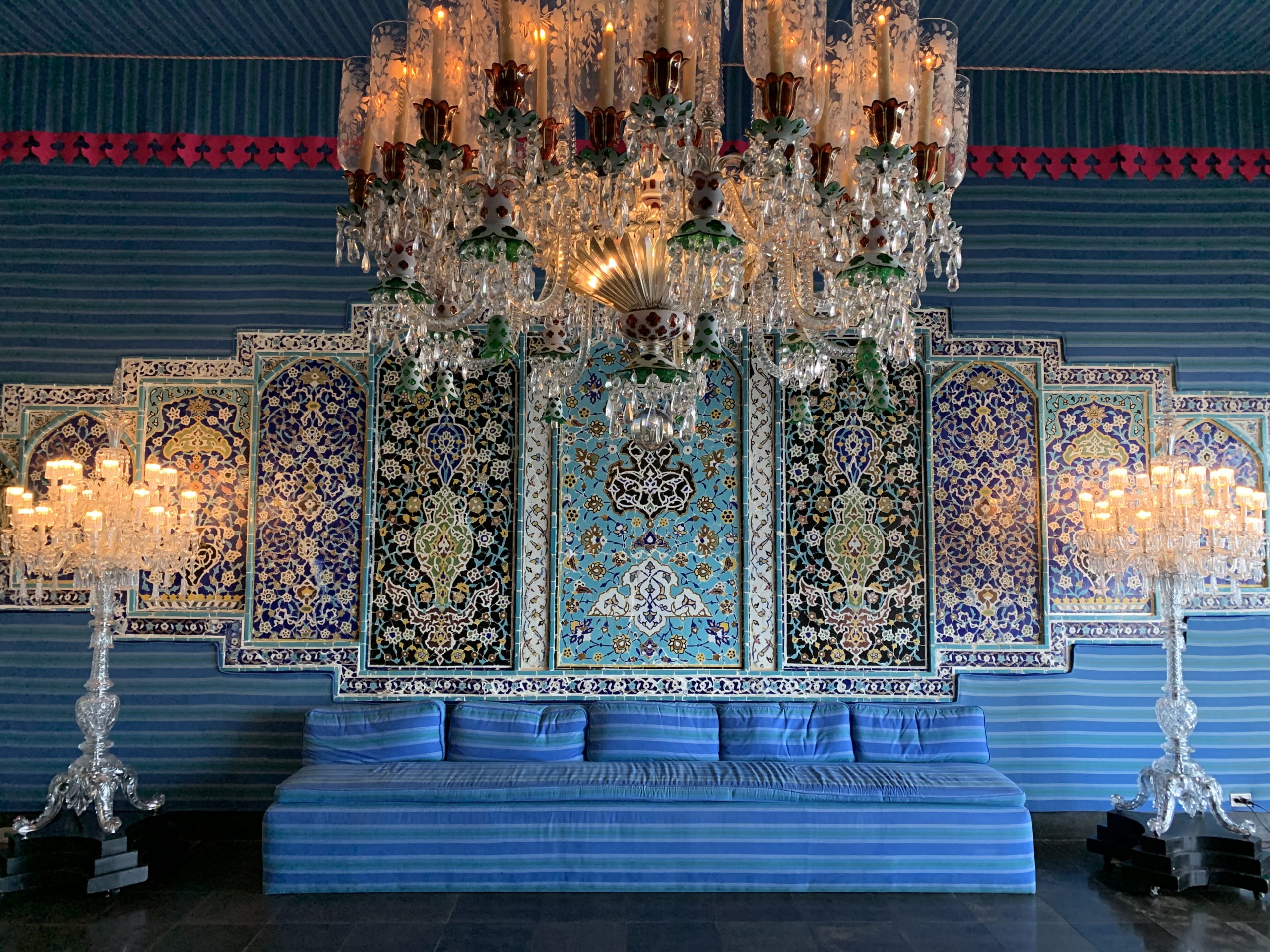 Interior of the Tent Room featuring a massive crystal chandelier, intricate blue floral wall patterns, and a long blue striped sofa.