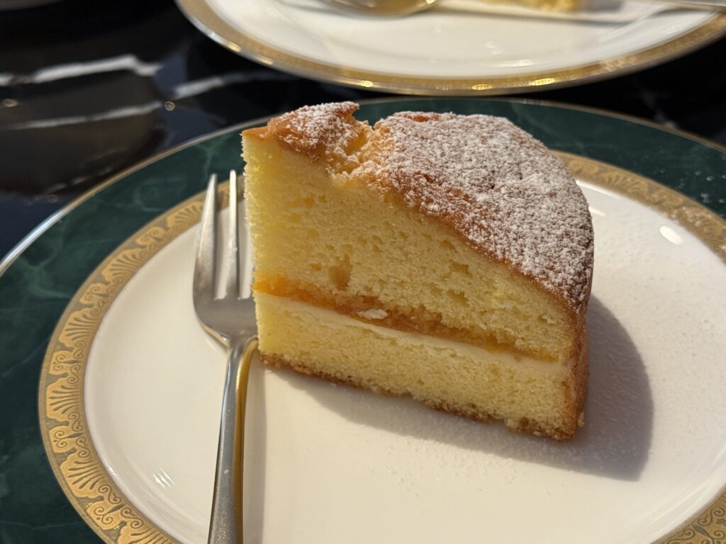 Close-up of a slice of Victoria sponge cake with powdered sugar on a green and gold rimmed plate with a fork