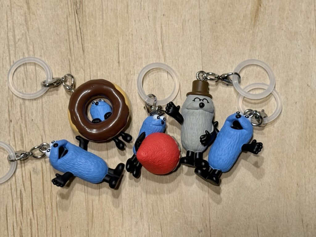 Four Puppet Sunsun capsule toy charms on a wooden table, including Sunsun with a donut and strawberry, and Non-Non