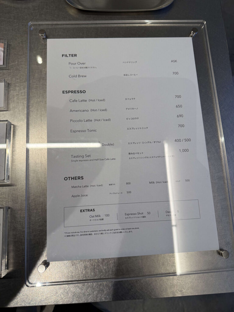 Cafe drink menu inside a clear acrylic frame on a metal counter