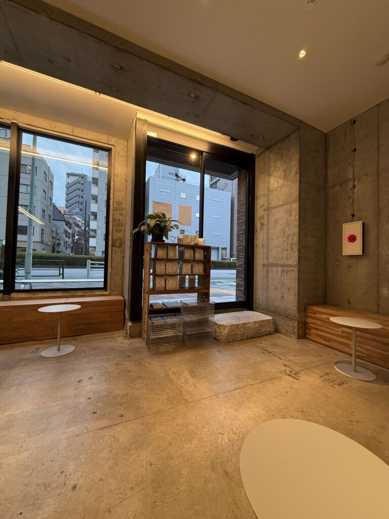 Interior of a modern cafe featuring exposed concrete walls, large windows, and wooden benches
