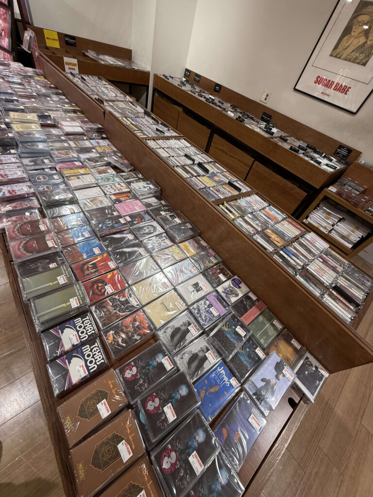 Rows of used cassette tapes densely packed on wooden shelves in a music store