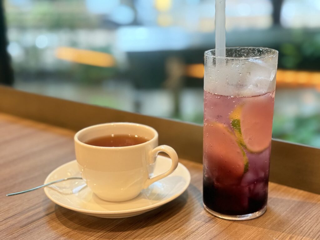 木製のテーブルの上に置かれた白いカップに入った温かい紅茶と、氷とライムのスライスが入った鮮やかなピンク色のソーダ