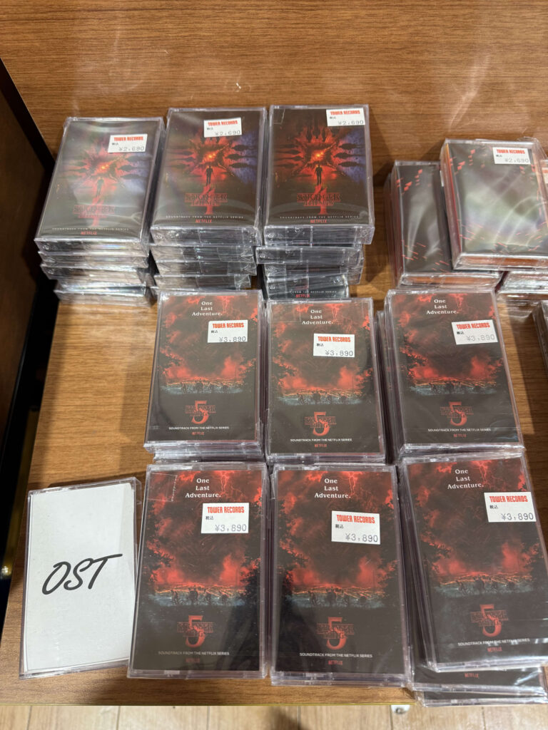 Stacks of Stranger Things soundtrack cassette tapes on a wooden shelf with Tower Records price tags