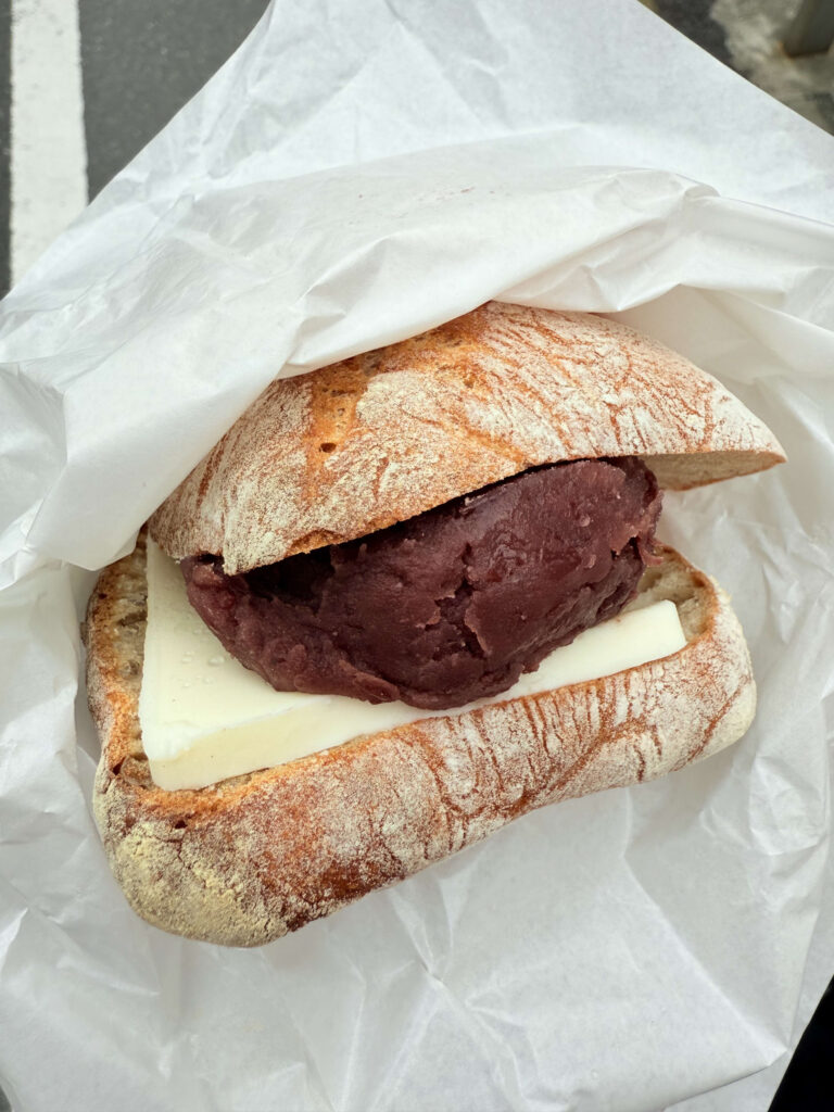 An-butter sandwich wrapped in white paper, featuring crusty bread filled with a thick slice of butter and generous sweet red bean paste