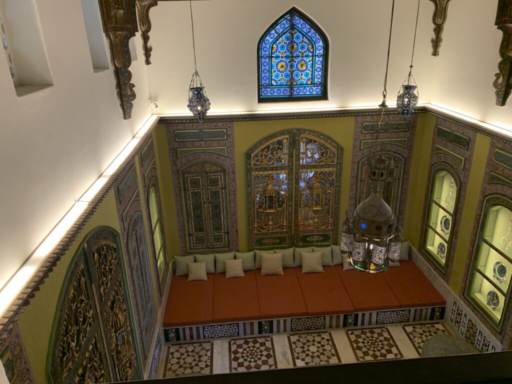 High-angle view of a luxurious interior featuring bright orange seating, geometric marble floors, and an arched stained-glass window