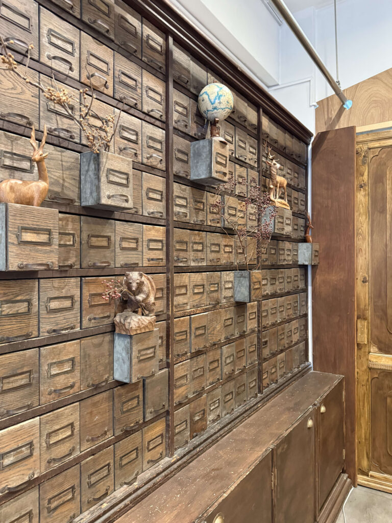 Floor-to-ceiling antique wooden apothecary drawers decorated with wooden deer, a bear carving, a globe, and dried flowers