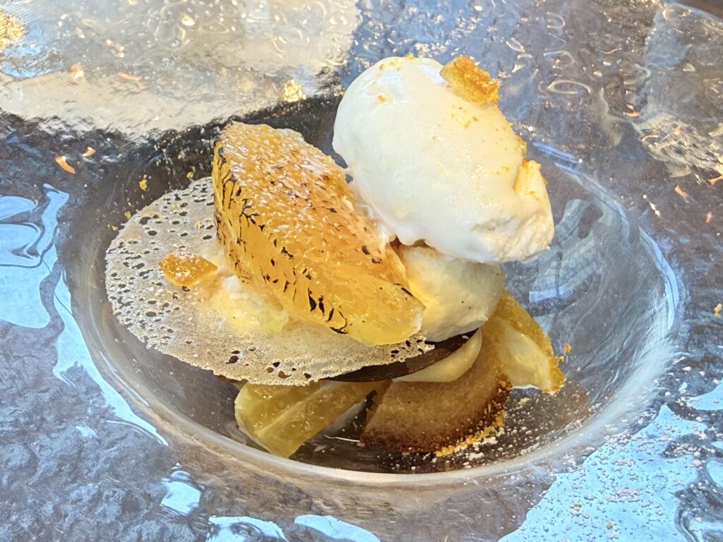 Decopon citrus and financier tart-style dessert topped with a scoop of ricotta milk sorbet in a textured glass bowl