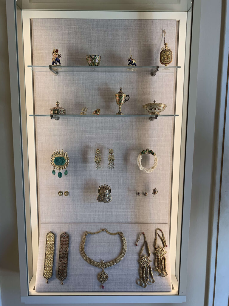 A display case filled with gold jewelry and ornaments featuring emeralds and pearls arranged on four shelves