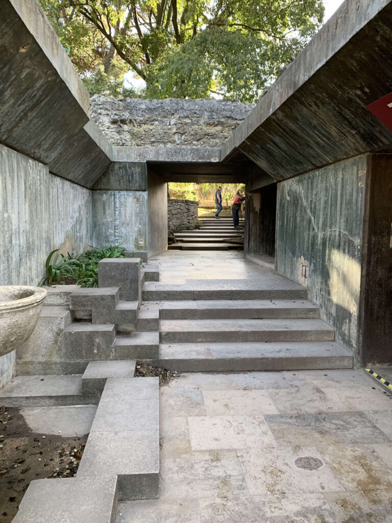 Modern concrete walkway and geometric stairs leading to an archaeological site shelter