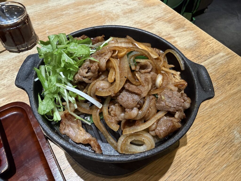 Kuroge Wagyu beef bulgogi served on a hot iron skillet with sautéed onions and fresh mizuna greens
