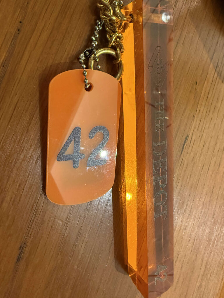 木のテーブルに置かれた、数字の42とTHE DEPOTの文字が入ったオレンジ色のアクリルキーホルダー