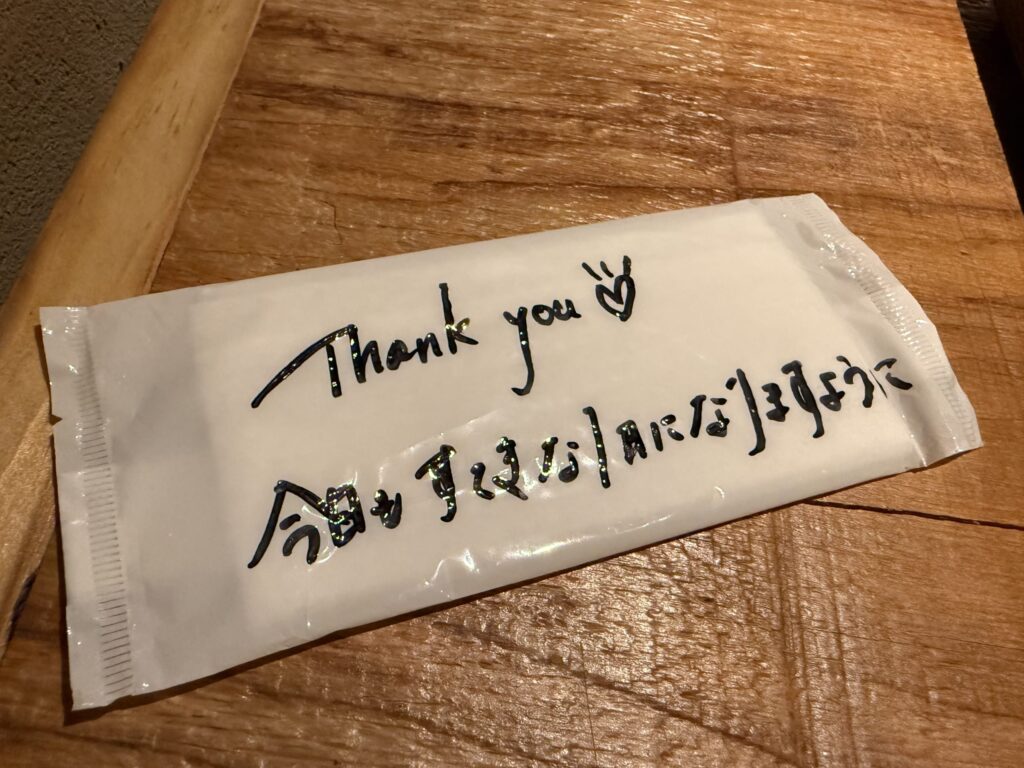 Wet wipe wrapper on a wooden table with a handwritten 'Thank you' message