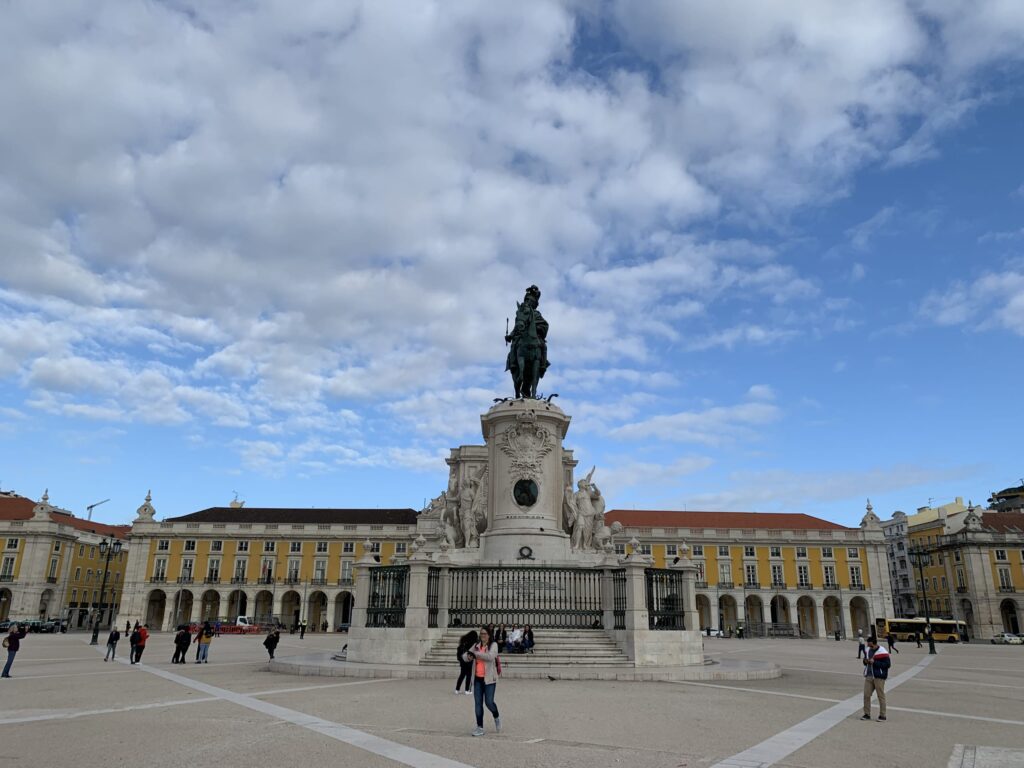 Equestrian statue of King José I in the center of Praça do Comércio in Lisbon, surrounded by yellow buildings with arcades under a blue sky with clouds