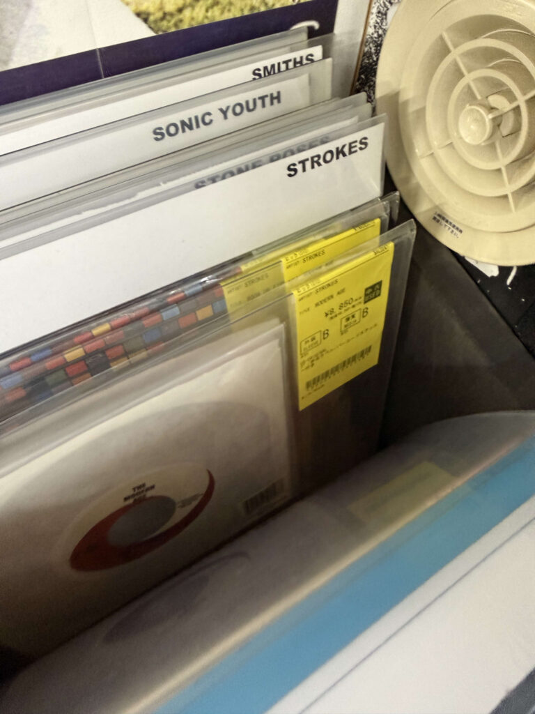 7-inch vinyl singles in a record store bin featuring The Strokes' 'Modern Age' and dividers for The Smiths and Sonic Youth