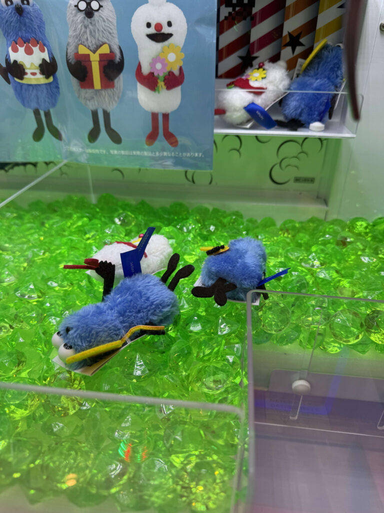 Puppet Sunsun plush toys resting on green plastic gems inside a claw machine